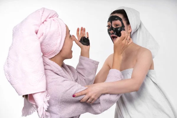 Setzt das Mädchen ihrer Schwester eine Kosmetikmaske auf. Sie haben Spaß und frönen dem Prozess. Leerer Hintergrund, gute Stimmung. Gesichtspflege. Schwestern. — Stockfoto