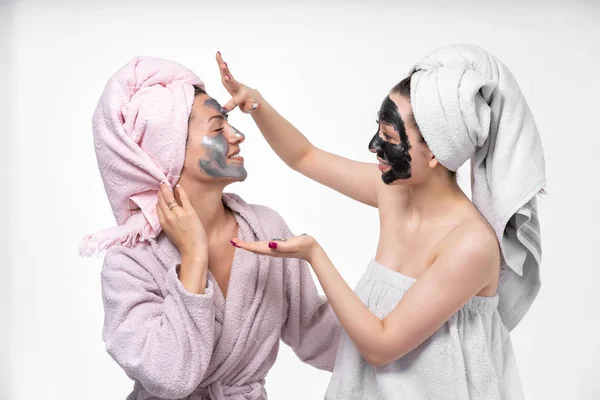La ragazza mette sua sorella una maschera cosmetica sul viso. Essi si divertono e indulgere nel processo. Sfondo vuoto, ottimo umore. Cura della pelle facciale. Sorelle . — Foto Stock