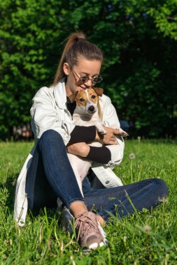 Genç bir kız parkta köpek Jack Russell Terrier 'a sarılıyor.