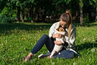 Genç bir kız parkta köpek Jack Russell Terrier 'a sarılıyor.