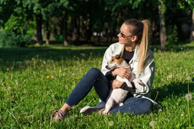 Genç bir kız parkta köpek Jack Russell Terrier 'a sarılıyor.