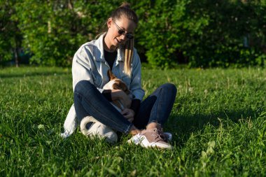 Genç bir kız parkta köpek Jack Russell Terrier 'a sarılıyor.