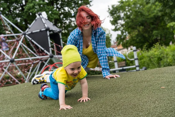 Küçük torunu dizlerinin üzerinde sürünerek çocuk parkında oynayan genç bir büyükanne.
