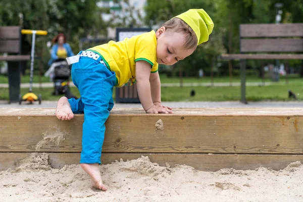 Um menino de dois anos de idade suavemente subindo em uma caixa de areia através de um freio alto — Fotografia de Stock