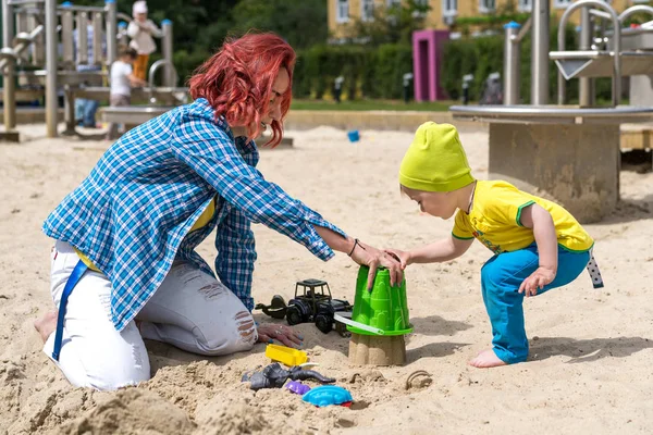 Jovem avó ensina seu neto dois anos de idade para fazer figuras de sua areia, jogar na caixa de areia no verão — Fotografia de Stock