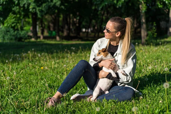 Genç bir kız parkta köpek Jack Russell Terrier 'a sarılıyor.