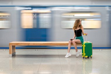küçük bir yeşil bavul ile genç bir güzel Avrupa kız tren bekliyor tren istasyonunda bir bankta oturuyor. Tema tek başına seyahat