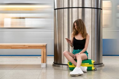 Kız 25 yaşında Metro İstasyonu, tren istasyonunda bankta dinlenmek için oturdu. O yeşil bir bavul ile seyahat.
