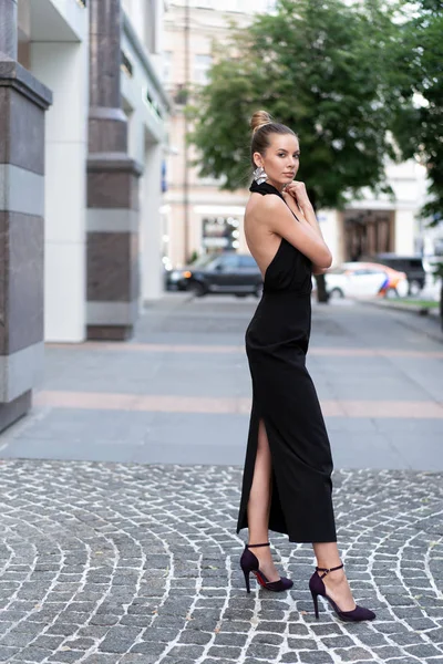 Schöne schlanke europäische Mädchen von 30 Jahren in einem schwarzen Kleid posiert auf der Straße in der Nähe von Boutiquen. schönes Wetter und gute Laune. Stylisches schönes Modell in vollem Wachstum. — Stockfoto