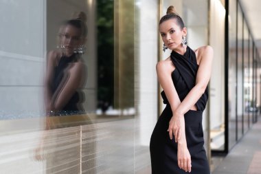 Güzel bir Avrupa modeli bir dükkan penceresi yakınında siyah bir elbise içinde poz olduğunu. Yansımasını görebilirsiniz. Reklam moda trendleri için şık bir atmosfer. Ortalama plan