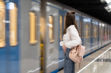 Uzun saçlı genç beyaz kız. Sırt çantasıyla. Metro istasyonunda dikilip treni bekliyorduk. Hareket gerçekliğinin etkilerini aktarmak için tren odak dışı..