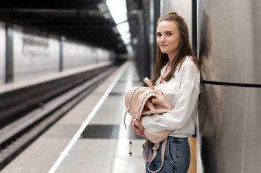 Pantolon ve sırt çantalı genç Avrupalı kız metro istasyonunda treni bekliyor. Hareketli arka plan, canlı bir atmosfer iletmek için bulanık. Bu harika bir fikir..