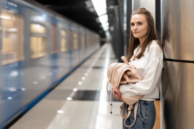 Avrupalı bir kız metro istasyonunda duran ve tren bekliyor bir sırt çantası ile. Tren, hareketin gerçekliğinin etkisini iletmek için odak dışında. Ana nesne bir kız.
