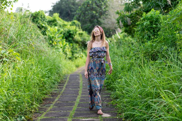 一个女孩走在一个绿色的公园里的石道上 年轻的欧洲人穿着长裙与大自然独处 一个人旅行 免版税图库照片