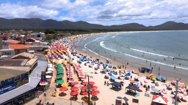 Florianpolis, Santa Catarina, Brezilya - 12 Ocak 2022 - Barra da Lagoa Plajı 'nın havadan görünüşü güneşli bir günde insan ve şemsiyelerle dolu.