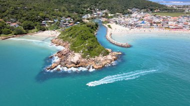 Florianpolis Santa Catarina Brezilya 'daki Barra da Lagoa Plajı' nın panoramik hava manzarası güneşli bir yaz gününde turkuaz mavi denizde yüzen yatıyla kalabalık plajla.