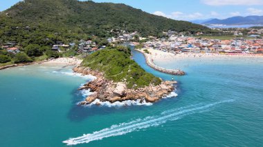 Florianpolis Santa Catarina Brezilya 'daki Barra da Lagoa Plajı' nın panoramik hava manzarası güneşli bir yaz gününde turkuaz mavi denizde yüzen yatıyla kalabalık plajla.