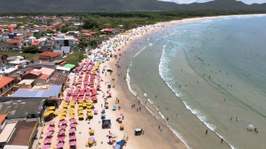 Florianpolis, Santa Catarina, Brezilya 'daki Barra da Lagoa plajının hava manzarası. Güneşli bir günde kum ve deniz insanlarla dolup taşıyor. Plajda şemsiyeli bir sürü turist.