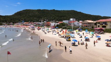 Florianpolis, Santa Catarina, Brezilya - Barra da Lagoa Sahili 'nin havadan görünüşü, güneşli bir günde insanlarla ve şemsiyelerle dolu.