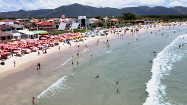 Florianpolis, Santa Catarina, Brezilya - Barra da Lagoa Sahili 'nin havadan görünüşü, güneşli bir günde insanlarla ve şemsiyelerle dolu.