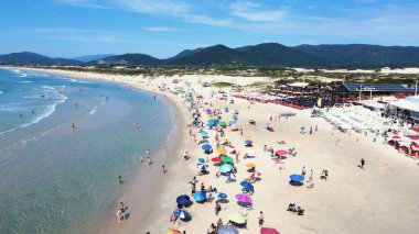 Florianopolis 'teki Joaquina Sahili' nin havadan görünüşü kumlu şerit ve turkuaz Atlantik Okyanusu plajı güneşli bir yaz gününde Santa Catarina 'da insanlarla ve şemsiyelerle dolu.