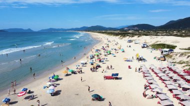 Florianopolis 'teki Joaquina Sahili' nin havadan görünüşü kumlu şerit ve turkuaz Atlantik Okyanusu plajı güneşli bir yaz gününde Santa Catarina 'da insanlarla ve şemsiyelerle dolu.
