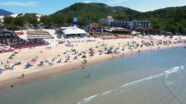 Florianopolis, Santa Catarina 'daki Joaquina Sahili' nin panoramik hava manzarası güneşli bir yaz gününde turkuaz mavisi deniz manzaralı insanlarla ve şemsiyelerle dolu..