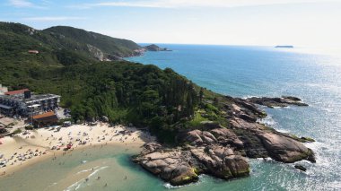 Florianopolis, Santa Catarina 'daki Joaquina Sahili' nin kayalık kıyı şeridinin panoramik manzarası, turkuvaz mavisi deniz ile güneşli bir yaz günü.