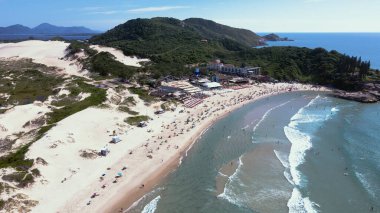 Florianopolis, Santa Catarina 'daki Joaquina Sahili' nin panoramik hava manzarası güneşli bir yaz gününde turkuaz mavisi deniz manzaralı insanlarla ve şemsiyelerle dolu..
