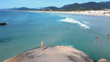 Florianopolis 'teki Joaquina Sahili' nin kayalık sahilindeki turkuaz okyanusa hayran kalan güzel bir kadının havadan görünüşü. Güneşli bir yaz gününde kalabalık bir plaj.