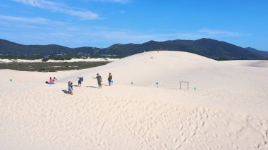 Florianpolis, Santa Catarina 'daki Joaquina Sahili' nin hava manzarası. İnsanlar kumda, kumsalda, sporda, kum tepeciklerinde, bitki örtüsünde, ekolojik ve turistik göllerde sörf yapıyor..