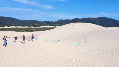 Florianpolis, Santa Catarina 'daki Joaquina Sahili' nin hava manzarası. İnsanlar kumda, kumsalda, sporda, kum tepeciklerinde, bitki örtüsünde, ekolojik ve turistik göllerde sörf yapıyor..