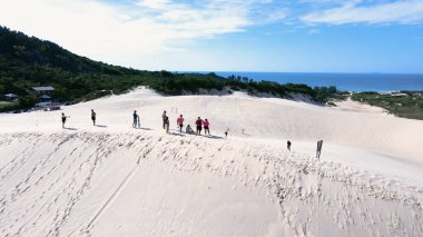 Florianpolis, Santa Catarina 'daki Joaquina Sahili' nin hava manzarası. İnsanlar kumda, kumsalda, sporda, kum tepeciklerinde, bitki örtüsünde, ekolojik ve turistik göllerde sörf yapıyor..