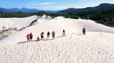 Florianpolis, Santa Catarina 'daki Joaquina Sahili' nin hava manzarası. İnsanlar kumda, kumsalda, sporda, kum tepeciklerinde, bitki örtüsünde, ekolojik ve turistik göllerde sörf yapıyor..