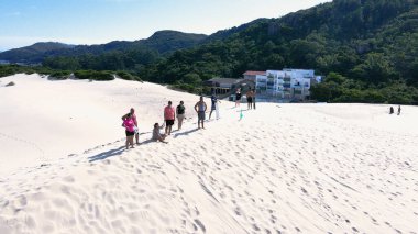 Florianpolis, Santa Catarina 'daki Joaquina Sahili' nin hava manzarası. İnsanlar kumda, kumsalda, sporda, kum tepeciklerinde, bitki örtüsünde, ekolojik ve turistik göllerde sörf yapıyor..
