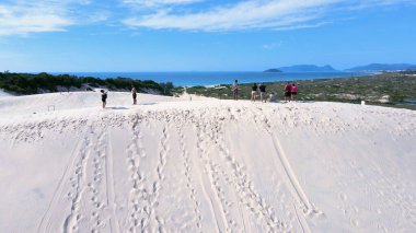 Florianpolis, Santa Catarina 'daki Joaquina Sahili' nin hava manzarası. İnsanlar kumda, kumsalda, sporda, kum tepeciklerinde, bitki örtüsünde, ekolojik ve turistik göllerde sörf yapıyor..