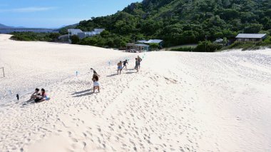 Florianpolis, Santa Catarina 'daki Joaquina Sahili' nin hava manzarası. İnsanlar kumda, kumsalda, sporda, kum tepeciklerinde, bitki örtüsünde, ekolojik ve turistik göllerde sörf yapıyor..