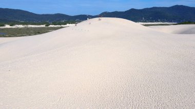Florianpolis, Santa Catarina 'daki Joaquina Sahili' nin hava manzarası. İnsanlar kumda, kumsalda, sporda, kum tepeciklerinde, bitki örtüsünde, ekolojik ve turistik göllerde sörf yapıyor..