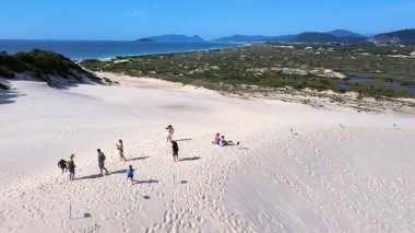 Florianpolis, Santa Catarina 'daki Joaquina Sahili' nin hava manzarası. İnsanlar kumda, kumsalda, sporda, kum tepeciklerinde, bitki örtüsünde, ekolojik ve turistik göllerde sörf yapıyor..