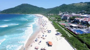 Brava Sahili 'nin kumları üzerinde hızla uçan hava manzarası. İnsanlar ve şemsiyelerle dolu. Florianpolis Santa Catarina Brezilya' da deniz kenarında birkaç bina ve ev..