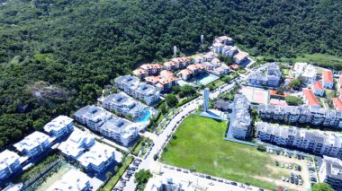 Florianpolis 'teki Praia Brava' nın havadan görünüşü, yaz mevsimi boyunca dağlarla ve Atlantik ormanlarıyla çevrili plajın önündeki çok sayıda apartman kompleksi ve yazlık ev..