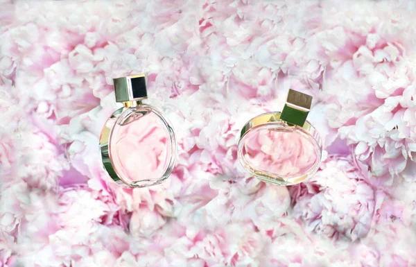 Botellas giratorias de perfume sobre fondo de flores rosas peonías con espacio para copiar. Perfumería, cosméticos, accesorios femeninos, colección de fragancias. Frasco de perfume delicado . — Foto de Stock