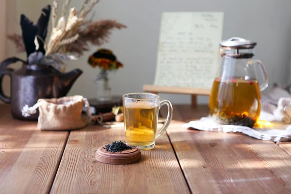 Традиционный геральный чай со стеклянным чайником, чашкой, сушеными бутонами роз. Цветы на деревянном столе дома, солнечный фон, выборочная фокусировка, копировальное пространство — стоковое фото
