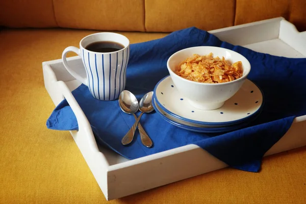 Bogate śniadanie kontynentalne na białej, drewnianej tabletce i żółtej kanapie. Francuskie chrupiące płatki kukurydziane, musli, słodkie jagody i gorąca kawa na smaczne poranne posiłki. Pyszny początek dnia.. — Zdjęcie stockowe