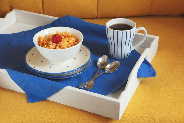 Rico desayuno continental en una tableta de madera blanca y un sofá amarillo. Maizales crujientes franceses, muesli, bayas dulces y café caliente para sabrosas comidas de la mañana. Delicioso comienzo del día . — Foto de Stock