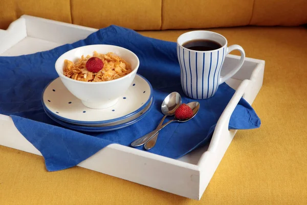 Rico desayuno continental en una tableta de madera blanca y un sofá amarillo. Maizales crujientes franceses, muesli, bayas dulces y café caliente para sabrosas comidas de la mañana. Delicioso comienzo del día . — Foto de Stock