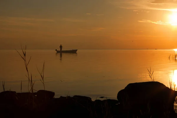 Рыбак у лодки на золотом закате моря. красивый и романтичный закат. силуэт пожарного с лодкой — стоковое фото
