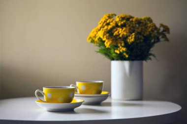 Klasik çay fincanı - İki sarı noktalı retro bardak ve sarı kasımpatı çiçekleri beyaz masada.