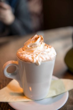 Ahşap masanın üzerinde bir fincan kapuçino. Bardaki sıcak kapuçino bardağı.
