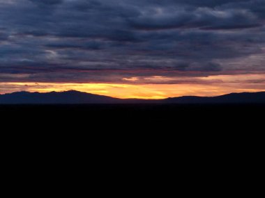Dağların siluetiyle yaklaşan gecenin gökyüzünün görüntüsü.